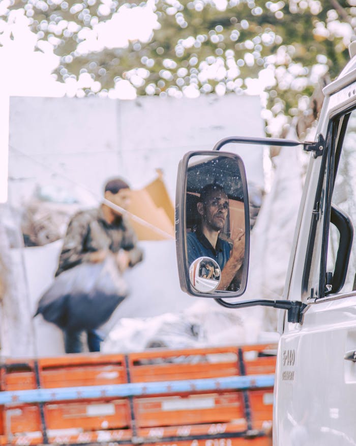Man's reflection in a side mirror of a truck with urban background, showcasing daily life.